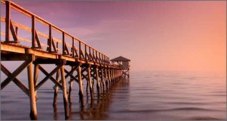 A scenic wooden pier extending into the ocean at sunset